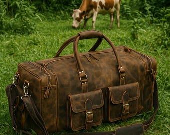 May include: A distressed brown leather duffel bag with two front pockets and a shoulder strap. The bag has a top handle and is sitting on green grass. A cow grazes in the background.