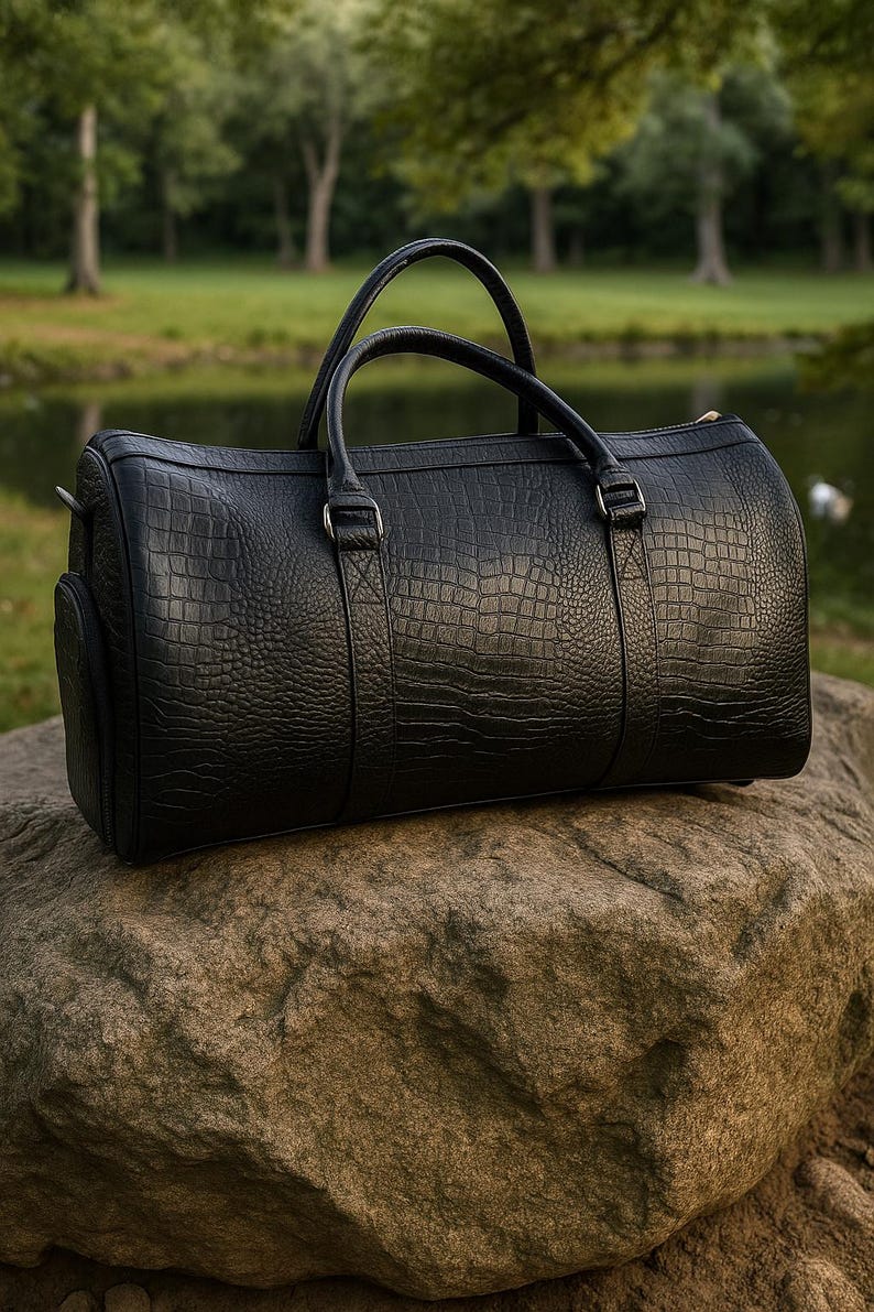 May include: A black duffel bag featuring a textured crocodile skin pattern, two top handles, and silver-toned metal hardware. The cylindrical bag has a structured design with reinforced stitching at the handle attachments and a side pocket.