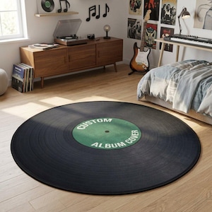 May include: A large, round black rug designed to resemble a vinyl record. The center label is green with the words "CUSTOM ALBUM COVER" in white. The rug is on a light wood floor, with a mid-century modern style room in the background.