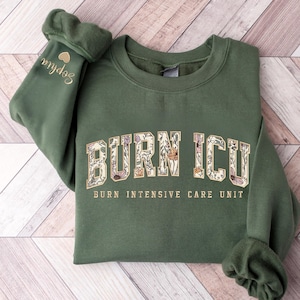 May include: A white ceramic mug with a black handle and the text "But First, Coffee" in a black, handwritten-style font. The mug is on a white surface.