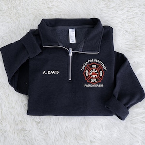 May include: A navy blue quarter-zip sweatshirt with the text "A. DAVID" on the left chest. The right chest features a custom fire department emblem in red, white, and black, with the words "CUSTOM FIRE DEPARTMENT" and "FIREFIGHTER/EMT".