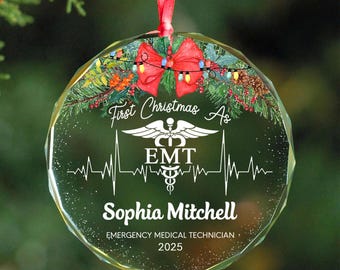 May include: A clear, round Christmas ornament with a red bow and festive lights. The ornament features the text "First Christmas As EMT" and the name "Sophia Mitchell" with the year 2025. A medical symbol and a heartbeat line are also present.