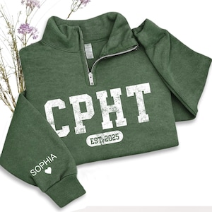 May include: A green quarter-zip sweatshirt with white block lettering that reads "CPHT" and "EST 2025". The sleeve has the name "Sophia" printed on it. The sweatshirt is made of a soft material.