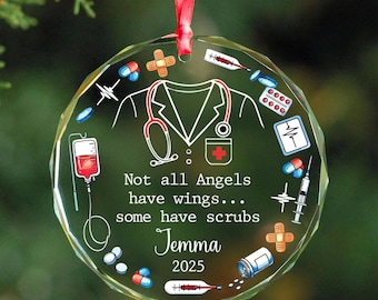 May include: A round, clear glass ornament with a red ribbon for hanging. The ornament features a white outline of a medical coat and stethoscope, surrounded by medical icons and the text "Not all Angels have wings... some have scrubs Jemma 2025."