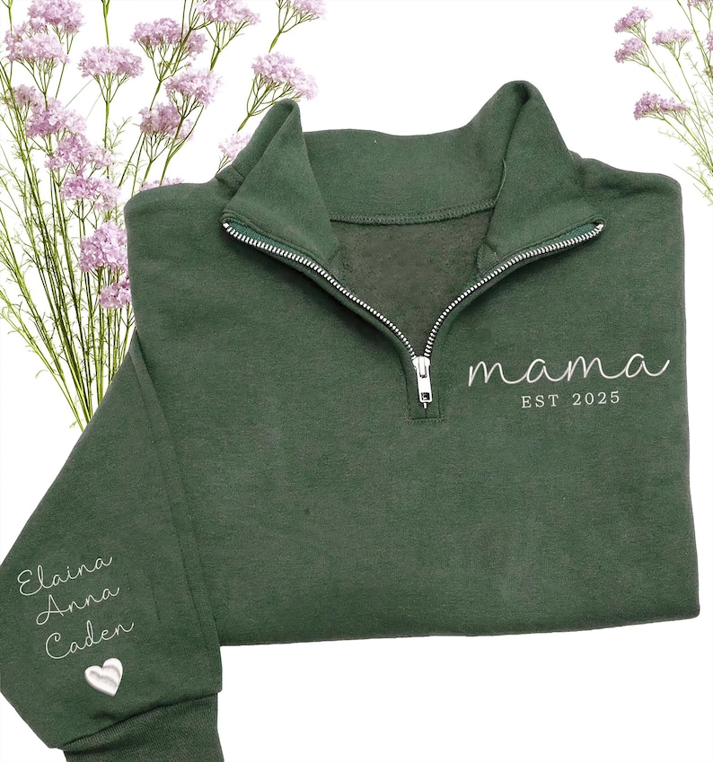 May include: A dark green sweatshirt with a quarter-zip neckline. The word "mama" and "EST 2025" are embroidered in white on the front. The left sleeve has the names "Elaina, Anna, Caden" embroidered in white, along with a white heart.