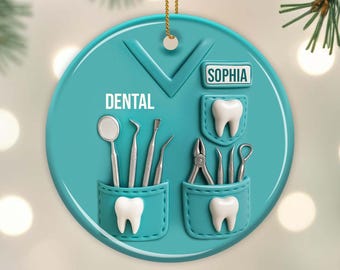 May include: A teal ceramic Christmas ornament shaped like a dentist's uniform, featuring the word "DENTAL" and the name "SOPHIA". It includes pockets with dental tools and tooth illustrations, suspended by a gold string.
