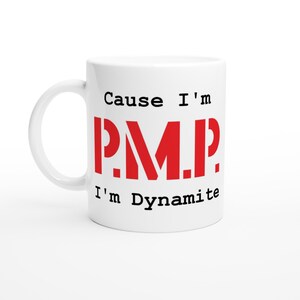 Könnte beinhalten: Weiße Keramik-Tasse mit dem Text "Cause I'm P.M.P. I'm Dynamite" in schwarzer und roter Schrift. Die Tasse hat einen gebogenen Henkel und ist für heiße oder kalte Getränke geeignet.