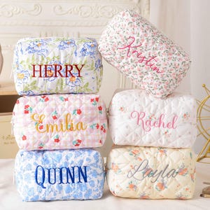 以下が含まれることがあります： HERRY、Emilia、QUINN、Kristin、Rachel、Laylaという刺繍入りの名前とユニークな花柄が特徴の、ファスナー付きキルティング生地ポーチ6点。ポーチは平らな場所に2列に積み重ねられています。