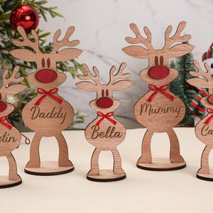 Puede incluir: Decoraciones navideñas de renos de madera con narices y lazos rojos. Cada reno tiene un nombre grabado: Justin, Daddy, Bella, Mummy y Camila. Decoración festiva navideña.