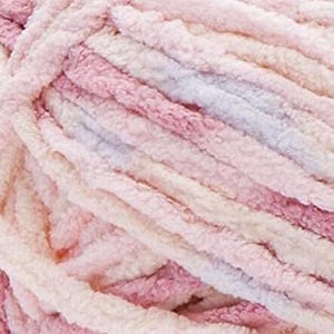May include: Close-up of a skein of soft, plush yarn in shades of pink, cream, and lavender. The yarn has a thick, textured appearance, ideal for knitting or crocheting projects. The colors blend together, creating a gradient effect.