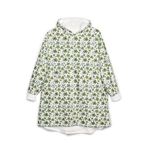 Może przedstawiać: Biały koc z kapturem z wzorem zielonych koniczynek i małych kwiatów. Kaptur i mankiety są białe. Koc jest przeznaczony do noszenia, z długimi rękawami i wygodnym, obszernym krojem.