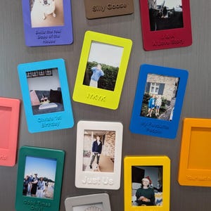 Può includere: Una collezione di colorate cornici fotografiche rettangolari con varie immagini e testo. Le cornici sono in tonalità di blu, giallo, verde, rosso e bianco. Il testo include "Olivia's 1st Birthday", "IYKYK" e "My Favourite People".