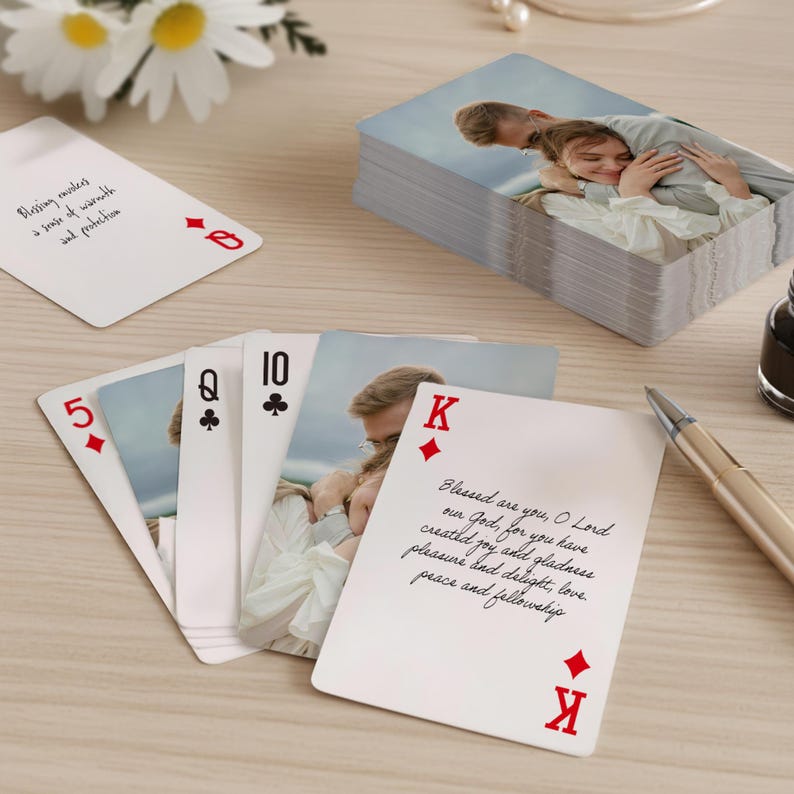 May include: A deck of custom playing cards featuring a photo of a couple. The cards are white with red suits and black numbers. The King of Diamonds card has a handwritten prayer. Other cards include the 5 of Hearts, Queen of Clubs, and 10 of Clubs.