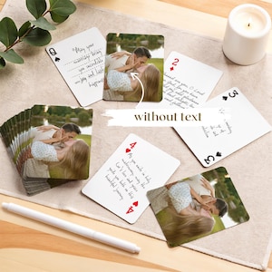 May include: A deck of playing cards with custom photos of a couple kissing. The cards are arranged on a beige surface with a white pen and a lit candle. The cards have different suit symbols and numbers.