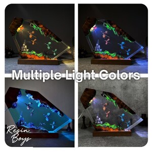 Puede incluir: L&aacute;mpara decorativa de resina con m&uacute;ltiples opciones de color de luz. Presenta una escena de fantas&iacute;a con dragones, un castillo y un paisaje. La base es de madera. El texto "Multiple Light Colors" y "Resin Boys" es visible.