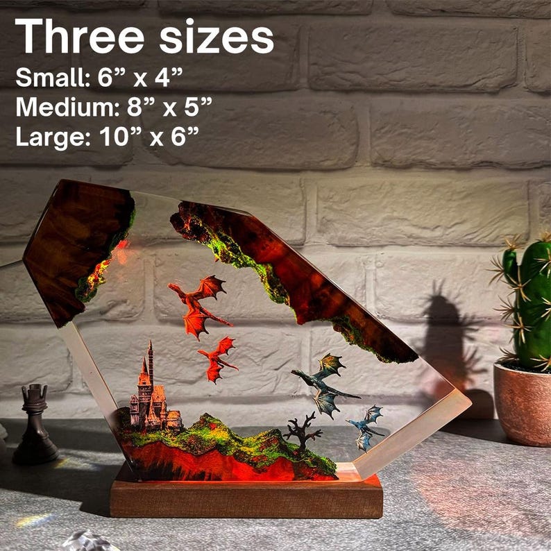 Puede incluir: L&aacute;mpara decorativa de resina con una escena de fantas&iacute;a que incluye un castillo, dragones y un paisaje monta&ntilde;oso. La l&aacute;mpara est&aacute; sobre una base de madera y est&aacute; disponible en tres tama&ntilde;os.