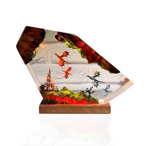 Puede incluir: Una pieza de arte de resina de tem&aacute;tica fant&aacute;stica que presenta un castillo, dragones y un paisaje. La obra de arte est&aacute; encerrada en un bloque de resina transparente y angular con una base de madera. Dragones rojos, verdes y azules vuelan.