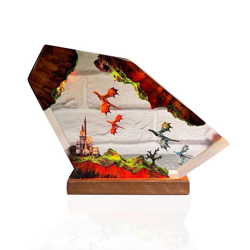 Puede incluir: Una pieza de arte de resina de tem&aacute;tica fant&aacute;stica que presenta un castillo, dragones y un paisaje. La obra de arte est&aacute; encerrada en un bloque de resina transparente y angular con una base de madera. Dragones rojos, verdes y azules vuelan.