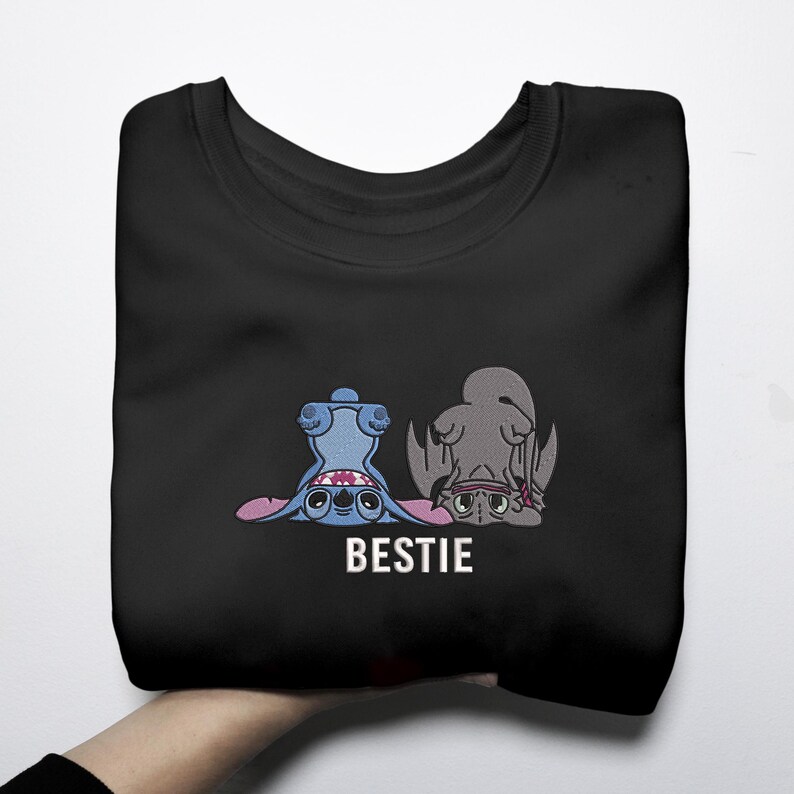 K&ouml;nnte beinhalten: Schwarzes Sweatshirt mit einer Cartoon-Grafik von zwei Figuren, eine blaue und eine graue, mit dem Wort "BESTIE" in Wei&szlig;. Die Figuren liegen und schauen den Betrachter an.