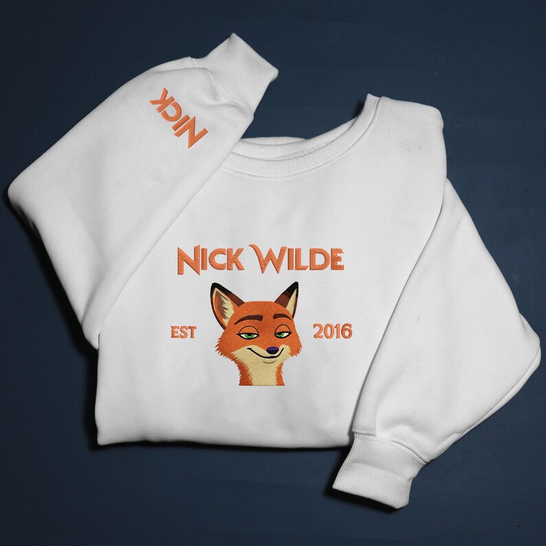 May include: White sweatshirt with an embroidered image of Nick Wilde, a fox character. The sweatshirt has the text "NICK WILDE" above the fox image, with "EST 2016" below. The word "NICK" is also embroidered on the sleeve.