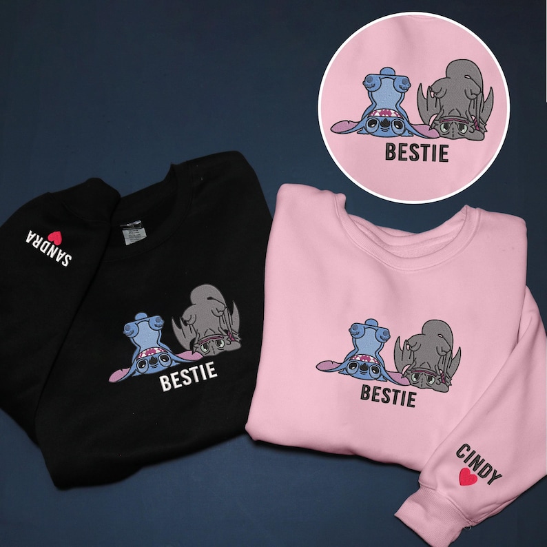 K&ouml;nnte beinhalten: Schwarze und rosa Sweatshirts mit einer Cartoon-Grafik von zwei Figuren, eine blaue und eine graue, mit dem Wort "BESTIE" darunter. Das schwarze Sweatshirt hat "SANDRA" auf dem &Auml;rmel aufgedruckt. Das rosa Sweatshirt hat "CINDY" auf dem &Auml;rmel aufgedruckt.