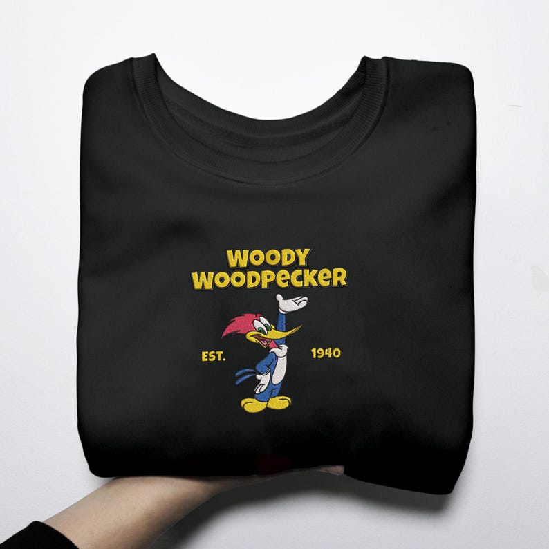 May include: Black sweatshirt featuring a Woody Woodpecker graphic. The design includes the text "WOODY WOODPECKER" in yellow, with an image of the cartoon character. The sweatshirt also has the text "EST. 1940".