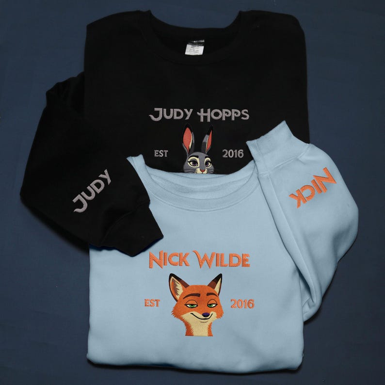 May include: Two sweatshirts, one black and one light blue, with embroidered designs. The black sweatshirt says "JUDY HOPPS" with a rabbit graphic and "EST 2016." The light blue sweatshirt says "NICK WILDE" with a fox graphic and "EST 2016."