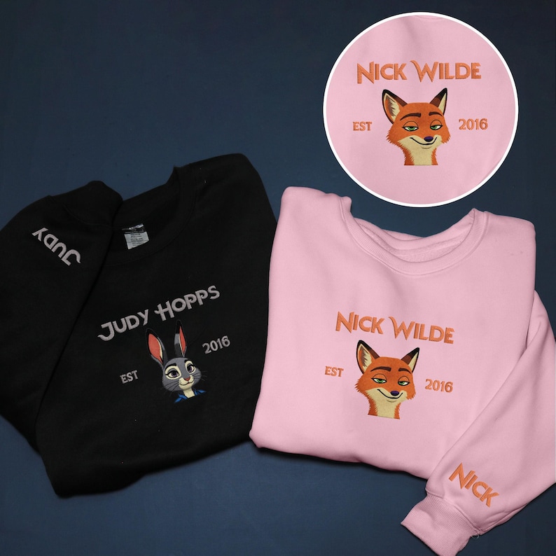 May include: Black and pink sweatshirts with character designs. The black sweatshirt features "Judy Hopps" and a bunny graphic. The pink sweatshirt displays "Nick Wilde" and a fox graphic. Both include "EST 2016".