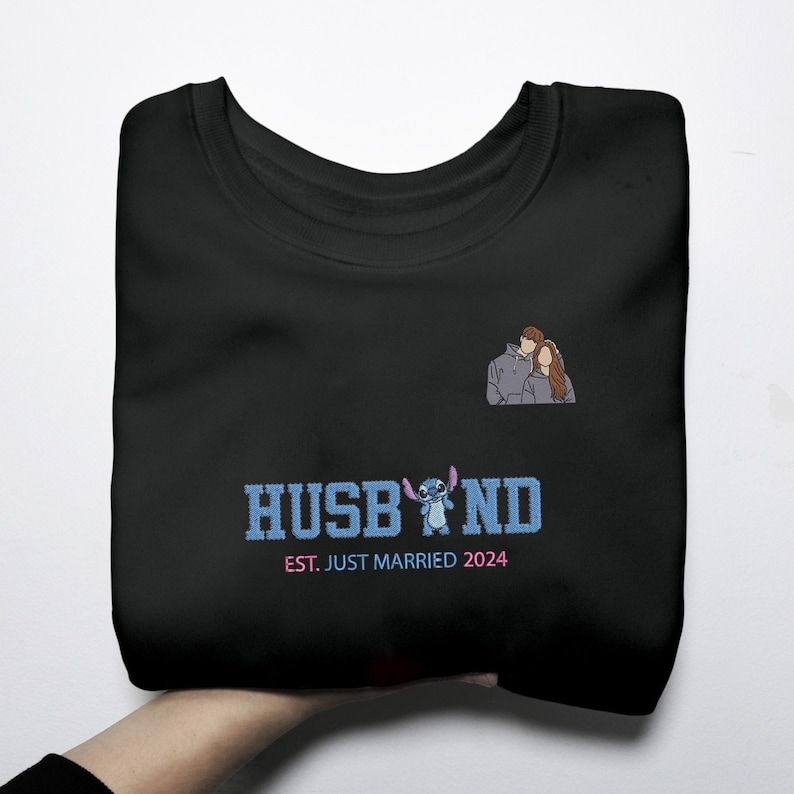 Puede incluir: Sudadera negra con la palabra "HUSBAND" en azul, con un personaje de dibujos animados y el texto "EST. JUST MARRIED 2024". Una peque&ntilde;a ilustraci&oacute;n de una pareja est&aacute; en la parte superior derecha. La sudadera est&aacute; doblada.