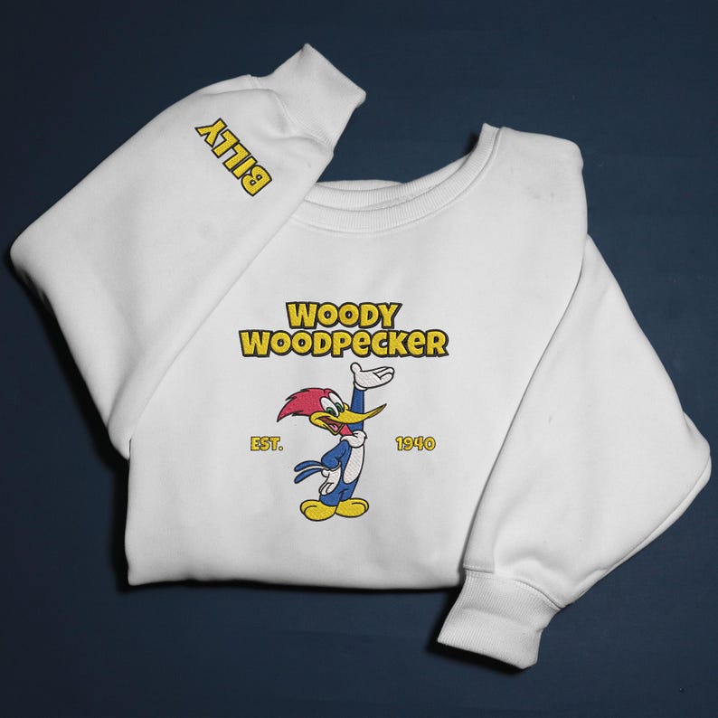 May include: White sweatshirt featuring the cartoon character Woody Woodpecker. The design includes the text "WOODY WOODPECKER" above the character, with "EST. 1940" below. The sleeve has the name "BILLY" in yellow.