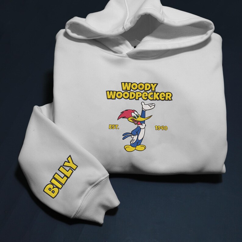 May include: White hoodie featuring the Woody Woodpecker logo in yellow and red. The sleeve displays the name "BILLY" in yellow. The hoodie has a drawstring hood and ribbed cuffs.