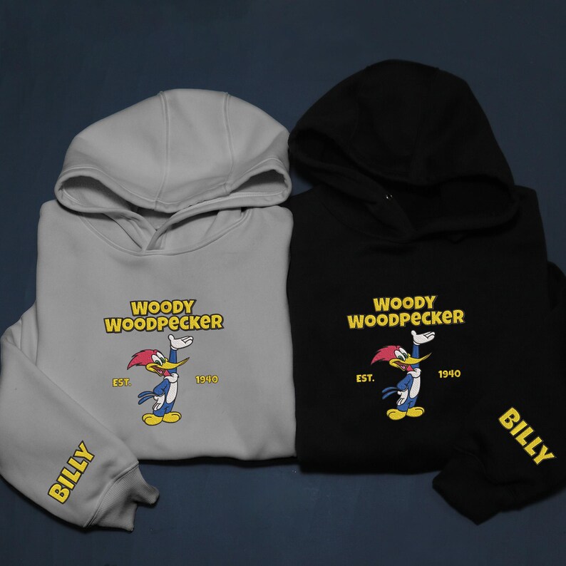 May include: Two hooded sweatshirts, one light gray and one black, featuring the Woody Woodpecker cartoon character. The sweatshirts have the Woody Woodpecker logo and the word "BILLY" on the sleeve.
