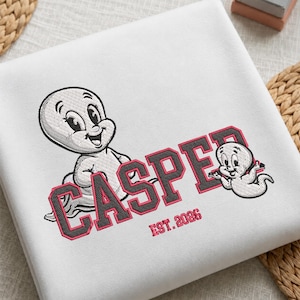 May include: A white sweatshirt featuring an embroidered design of two cartoon ghosts. The larger ghost is on the left, and the smaller one is on the right. The text CASPER is embroidered in large block letters with red outlines, and EST. 2026 is below.