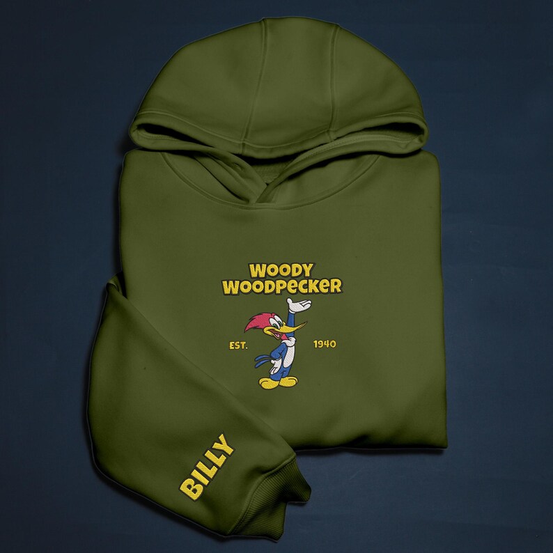 May include: Olive green hoodie featuring the cartoon character Woody Woodpecker. The hoodie has the text "WOODY WOODPECKER" in yellow, with the character illustration and the year "1940". The sleeve reads "BILLY" in yellow.