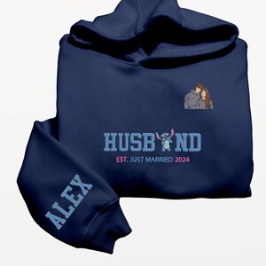 Puede incluir: Sudadera con capucha azul marino con la palabra "HUSBAND" en azul claro, con un personaje de dibujos animados. La manga muestra el nombre "ALEX" en azul claro. La sudadera tambi&eacute;n tiene el texto "EST. JUST MARRIED 2024" y una ilustraci&oacute;n de pareja.