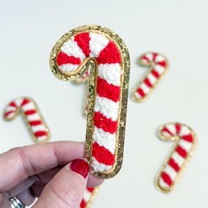 May include: Five red and white striped candy cane shaped patches with gold glitter trim. The patches are made of felt and are perfect for adding a festive touch to crafts and projects.
