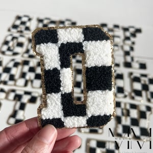 May include: A black and white checkered letter D with a gold glitter outline. The letter is made of a fluffy material and is perfect for adding a touch of personality to any project.
