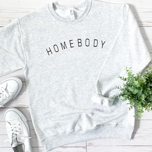 Puede incluir: Una sudadera gris con el texto "HOMEBODY" impreso en negro en la parte delantera.