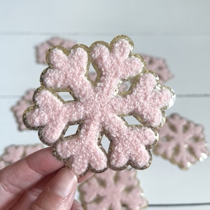 May include: Pink and gold glitter snowflake ornaments. The snowflakes are fuzzy and have a gold glitter outline.