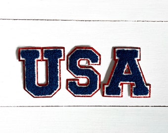 May include: USA spelled out in blue felt letters with red outlines. The letters are on a white wooden background.