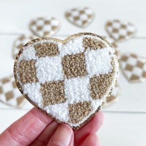 May include: A gold heart-shaped patch with a white and brown checkered pattern. The patch is made of a fluffy, textured material.