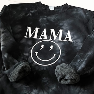 May include: Black tie-dye sweatshirt with a white smiley face with lightning bolts for eyes and the word "MAMA" above it.
