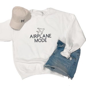 Puede incluir: Sudadera blanca con un gr&aacute;fico de avi&oacute;n negro y el texto "MODO AVI&Oacute;N".