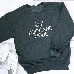 Puede incluir: Una sudadera gris oscuro con el texto "MODO AVI&Oacute;N" en letras blancas y un icono de avi&oacute;n blanco sobre el texto.