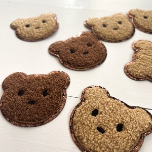 May include: A collection of brown and beige fuzzy bear appliques with a copper glitter trim. The bears have embroidered eyes and noses.