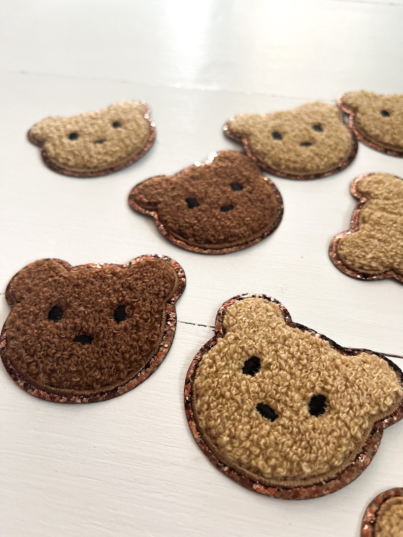 May include: A collection of brown and beige fuzzy bear appliques with a copper glitter trim. The bears have embroidered eyes and noses.