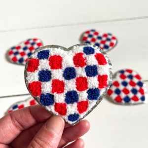 May include: A set of four red, white, and blue checkered heart-shaped patches. The patches are made of a soft, fuzzy material and have a silver glitter border.