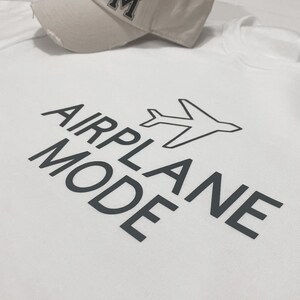 Puede incluir: Camiseta blanca con texto negro que dice "MODO AVI&Oacute;N" y un peque&ntilde;o gr&aacute;fico de avi&oacute;n.