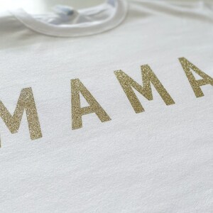 May include: White t-shirt with the word "MAMA" in gold glitter lettering.