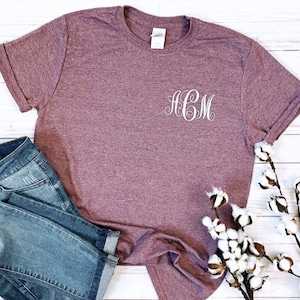 May include: A mauve t-shirt with a white monogram "HCM" embroidered on the front.